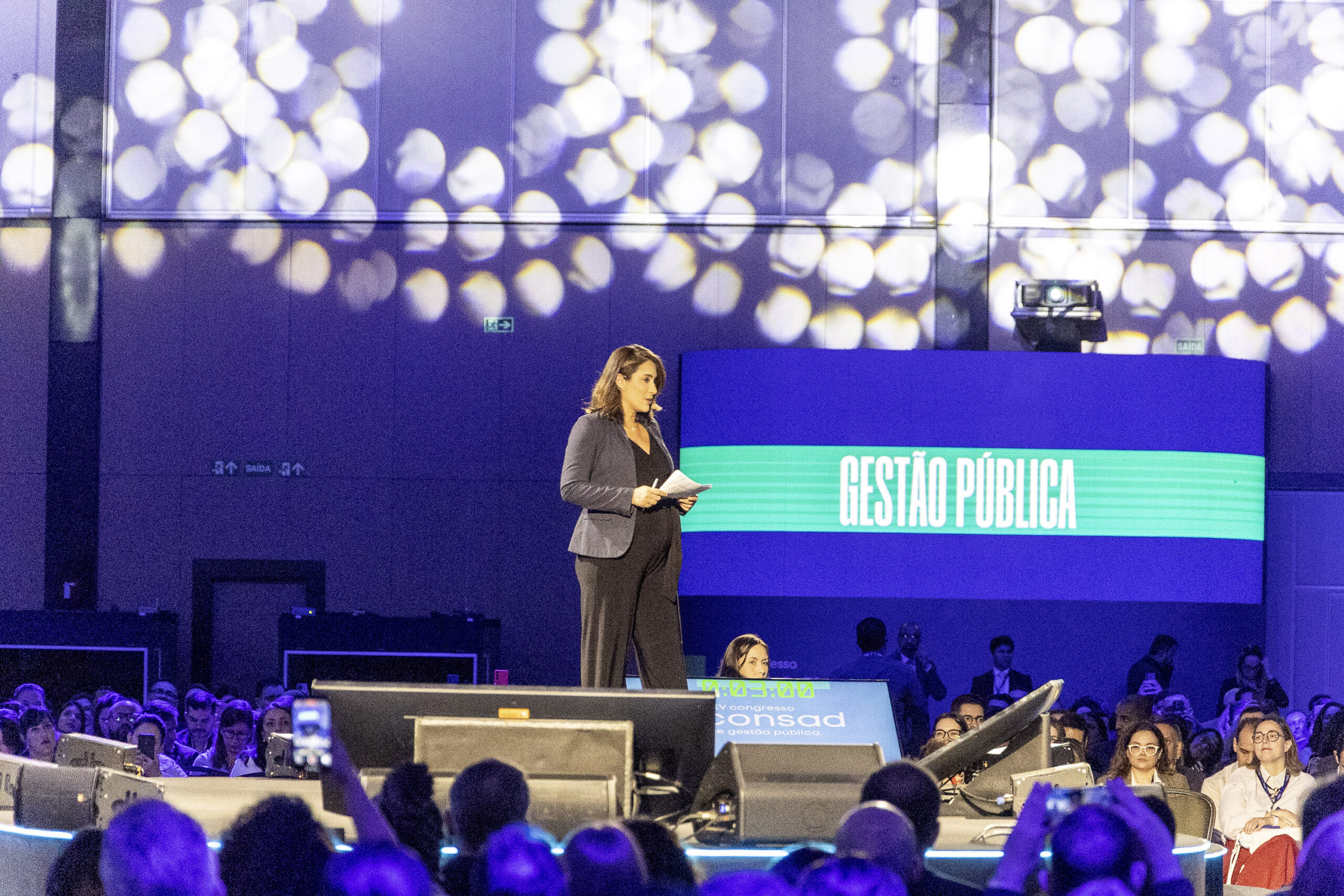 Palestrante feminina em congresso corporativo com luzes bokeh ao fundo
