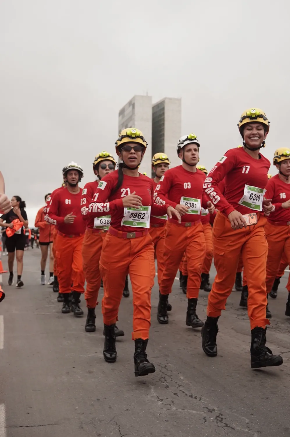 Bombeiros de uniforme laranja correndo em forma&ccedil;&atilde;o